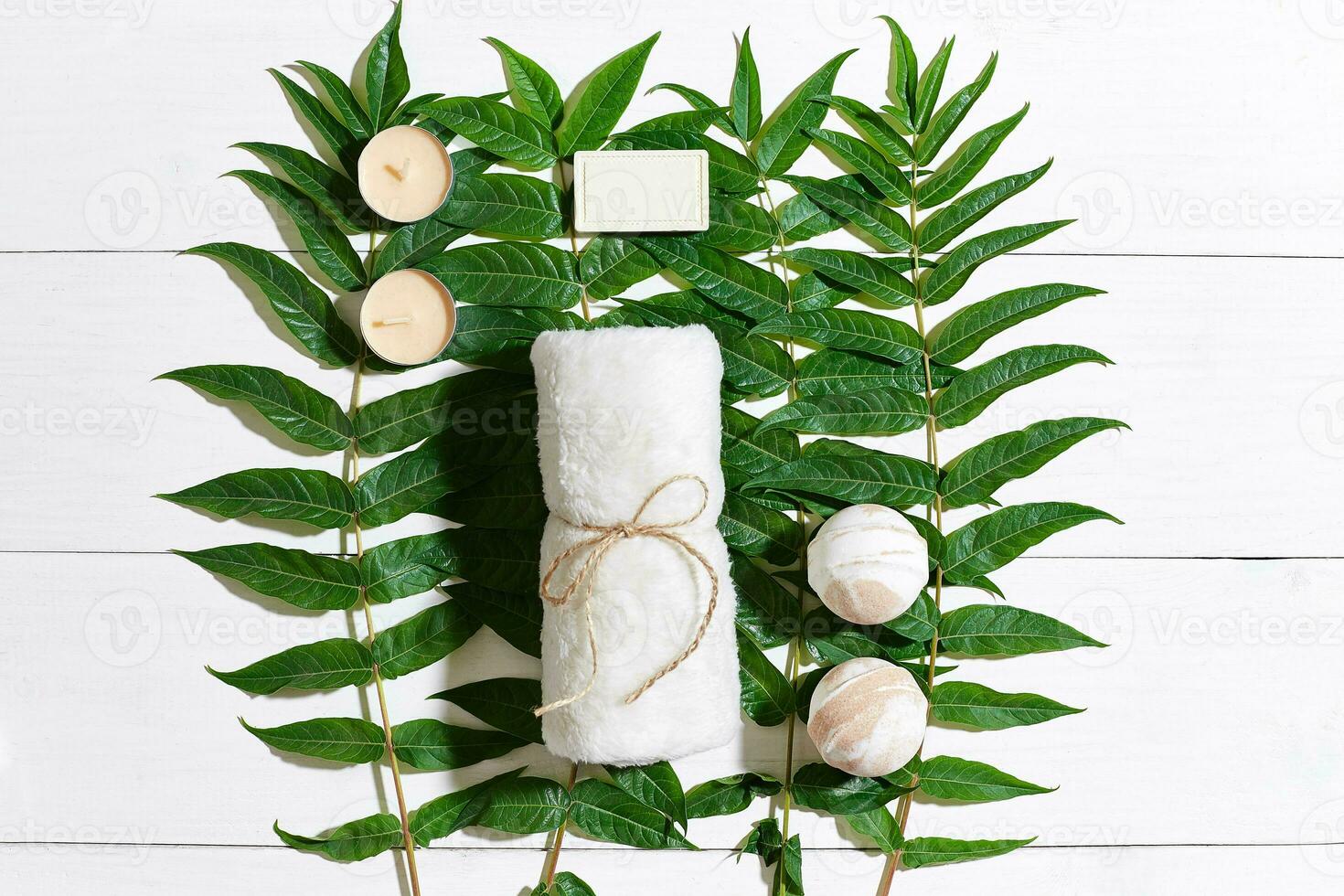 Spa set with towel and soap on white wooden background with green leaves photo