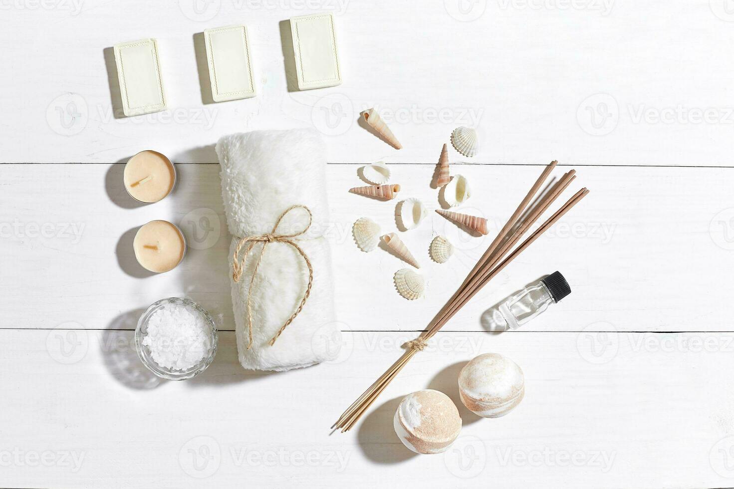 Spa set with sea salt, essential oil, soap and towel decorated with seashells on white wooden background photo
