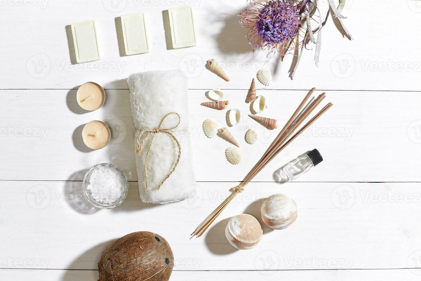 Spa set with sea salt, essential oil, soap and towel decorated with dry flower on white wooden background photo