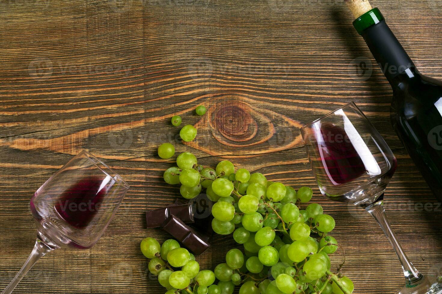 Red wine bottle, grape, chocolate and glasses over wooden table. Top view with copy space photo