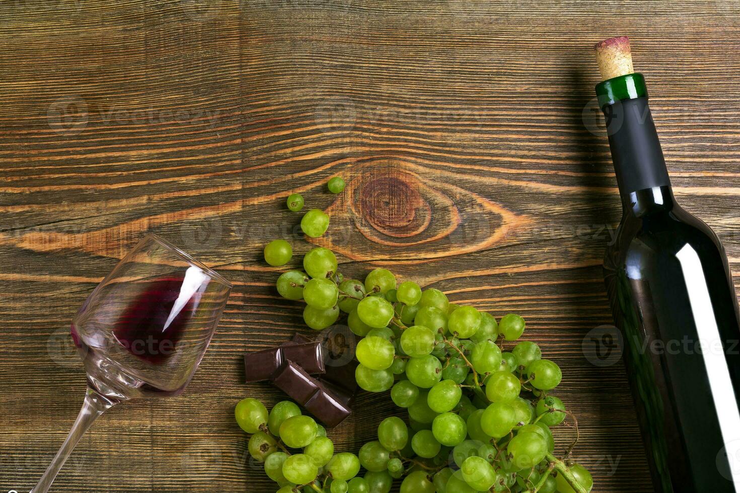 Red wine bottle, grape, chocolate and glasses over wooden table. Top view with copy space photo