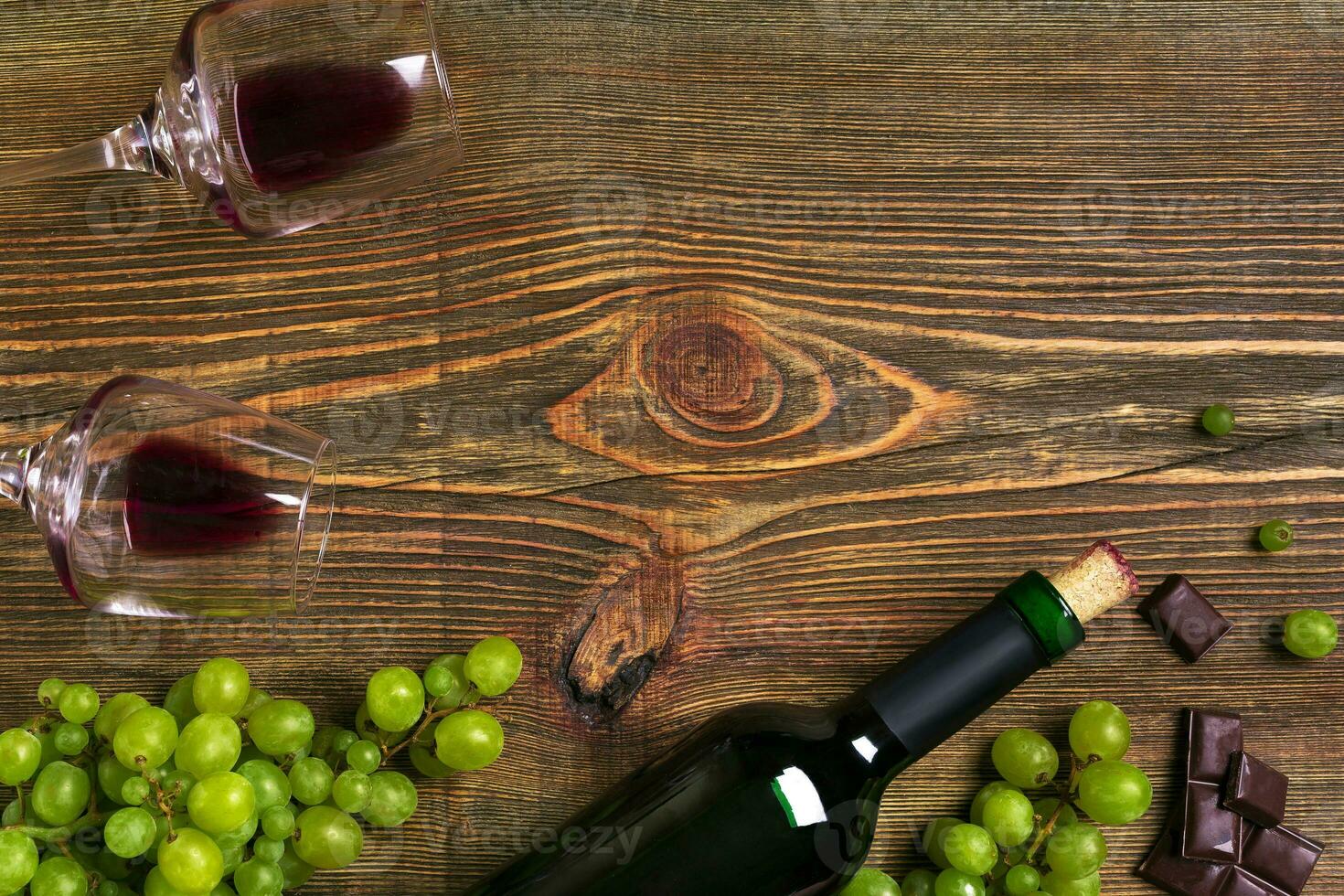 Red wine bottle, grape, chocolate and glasses over wooden table. Top view with copy space photo