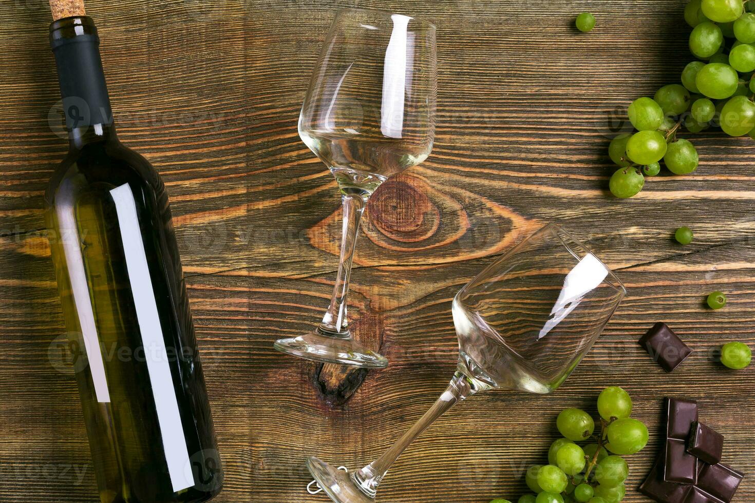 White wine bottle, grape, chocolate and glasses over wooden table. Top view with copy space photo