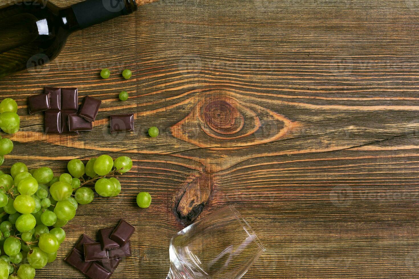 White wine bottle, grape, chocolate and glasses over wooden table. Top view with copy space photo