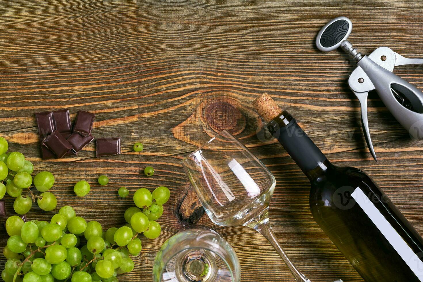 White wine bottle, grape, chocolate and glasses over wooden table. Top view with copy space photo