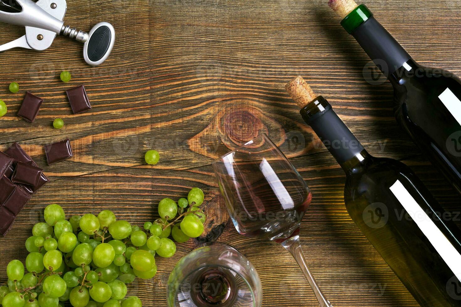 Bottles and glasses of wine, chocolate and ripe grapes on wooden background photo