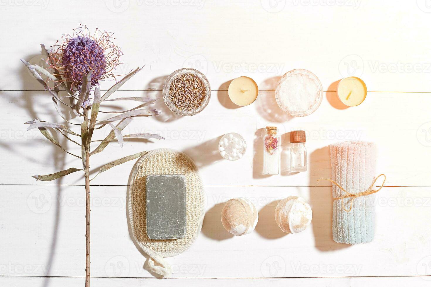 Spa set with sea salt, essential oil, soap and towel decorated with dry flower on white wooden background. Sun flare photo