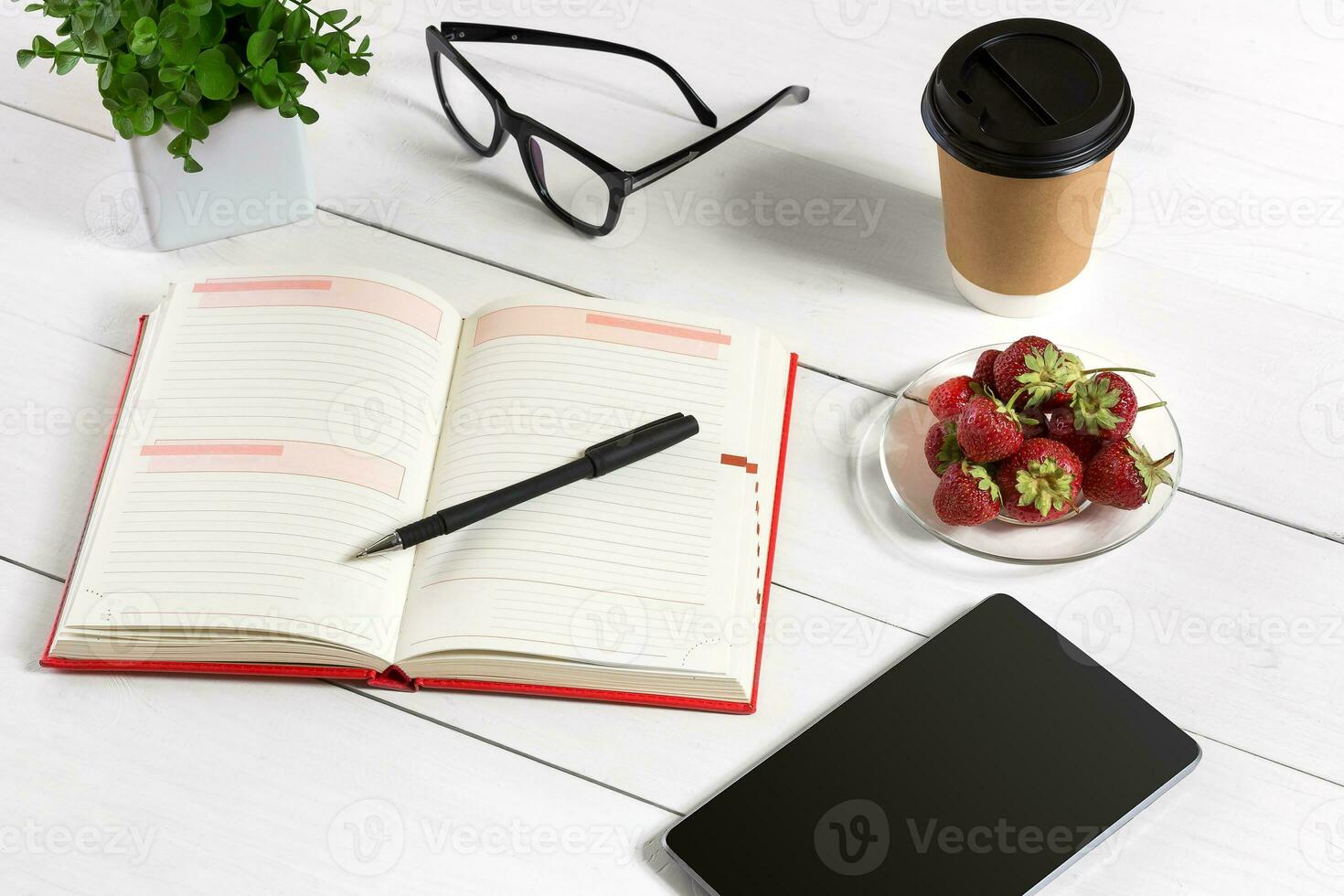 Office table desk with set of supplies, white blank notepad, cup, pen, tablet, glasses, flower on white background. Top view photo