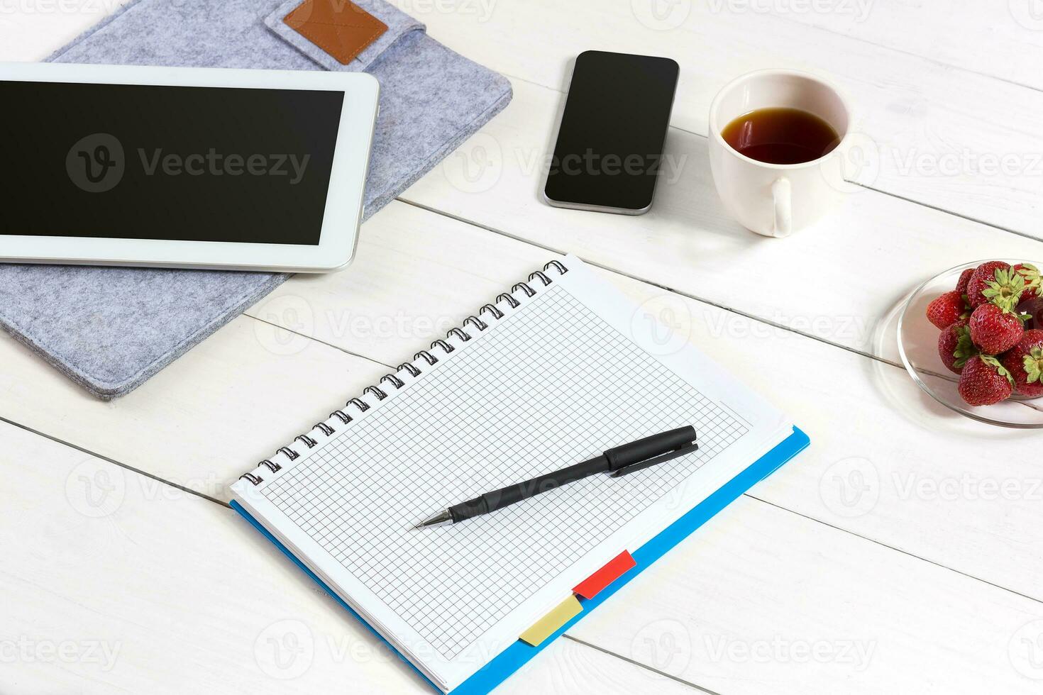 Office table desk with set of supplies, white blank notepad, cup, pen, tablet on white background. Top view photo