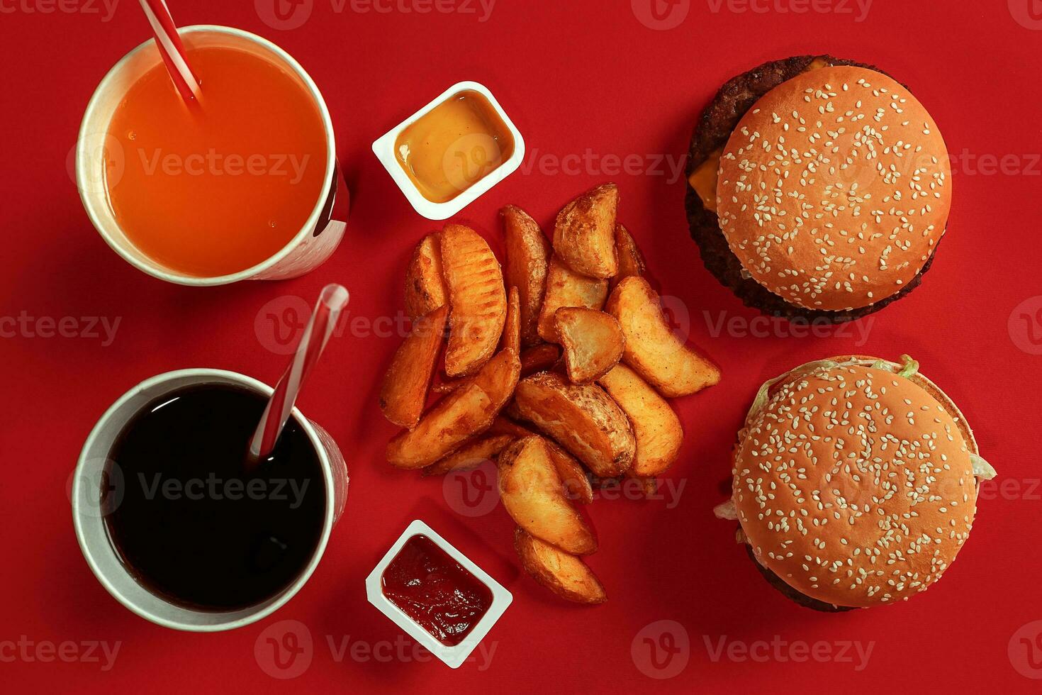 Two hamburgers and french fries, sauces and drinks on red background. Fast food. Top view, flat lay with copyspace photo