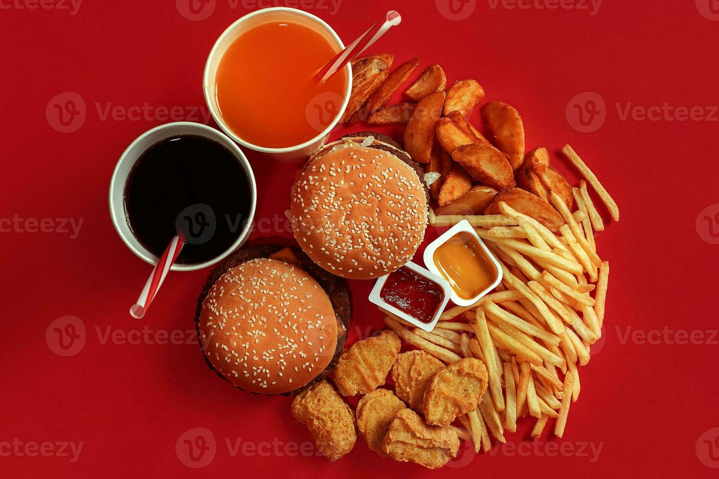 Two hamburgers and french fries, sauces and drinks on red background. Fast food. Top view, flat lay with copyspace photo