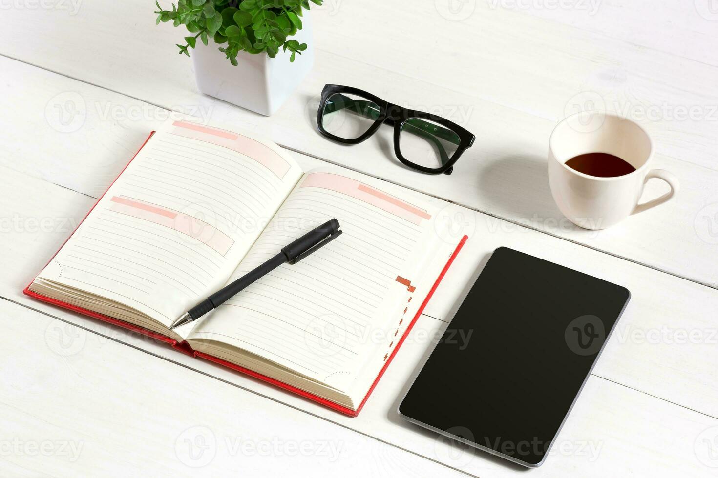 Office table desk with set of supplies, white blank notepad, cup, pen, tablet, glasses, flower on white background. Top view photo