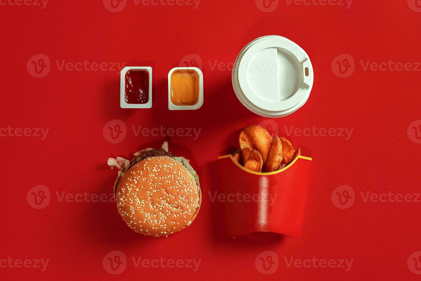 Fast food dish top view. Meat burger, potato chips and glass of drink on red background. Takeaway composition. photo