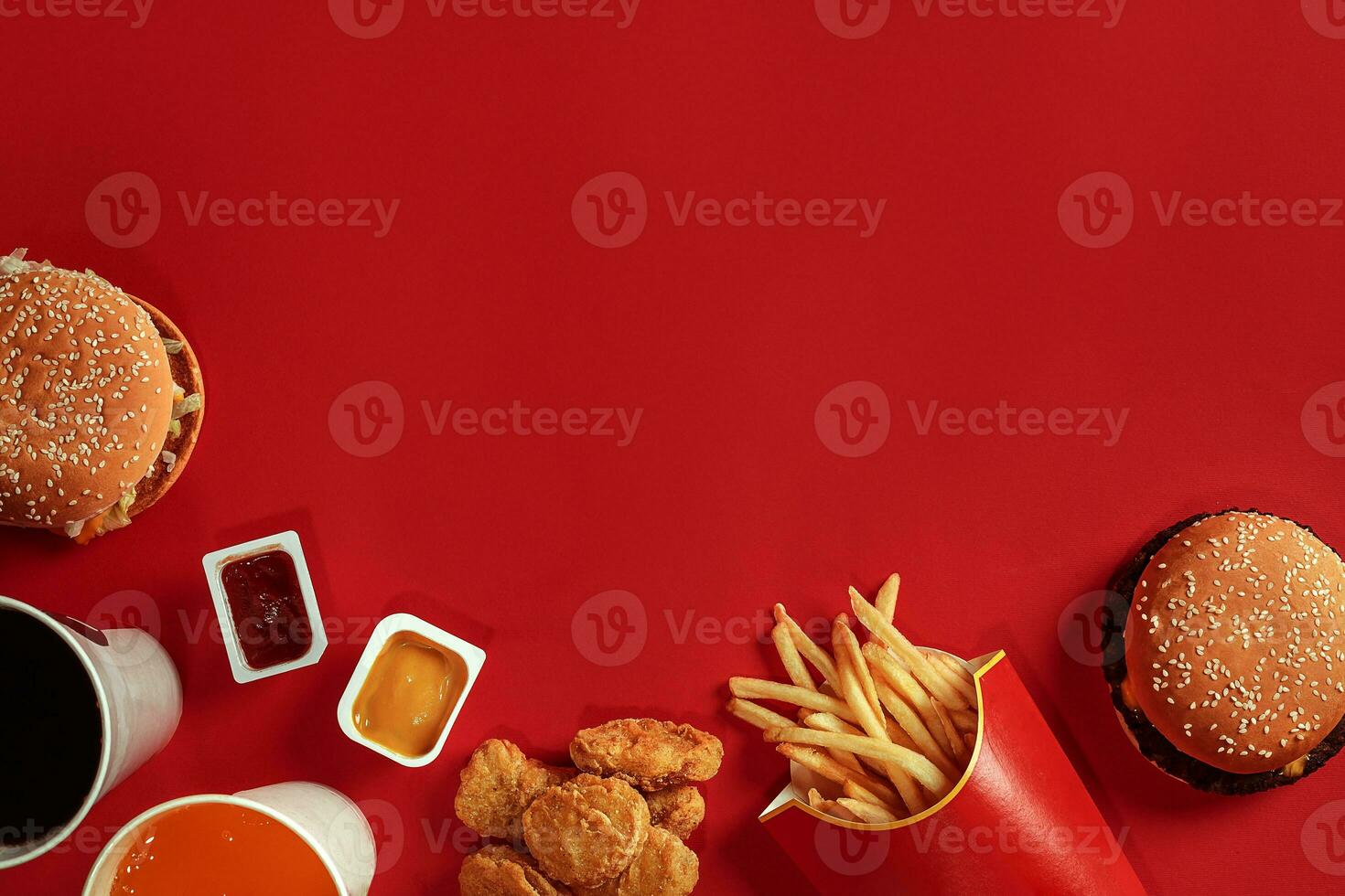 Two hamburgers and french fries, sauces and drinks on red background. Fast food. Top view, flat lay with copyspace photo