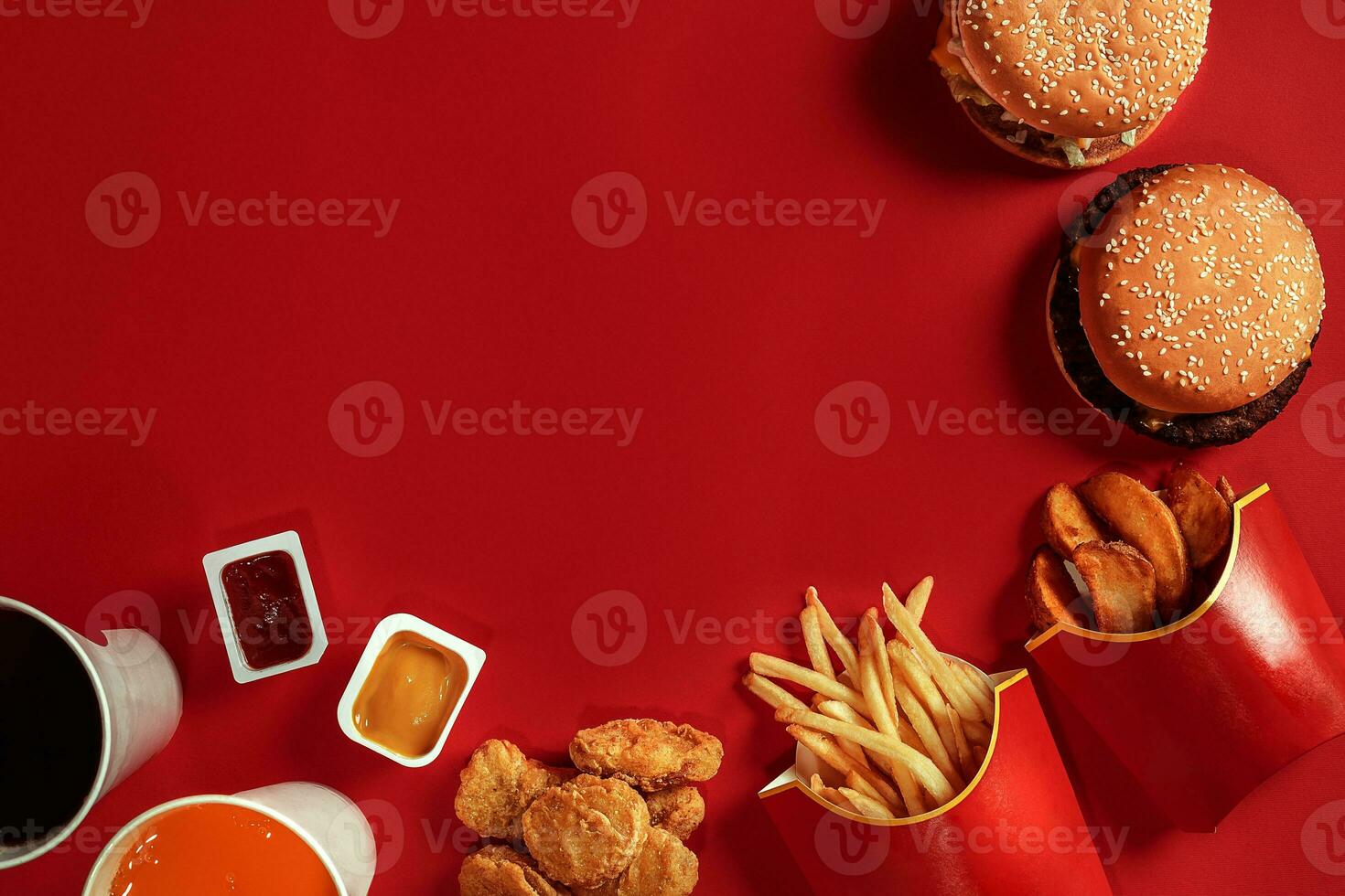 Two hamburgers and french fries, sauces and drinks on red background. Fast food. Top view, flat lay with copyspace photo