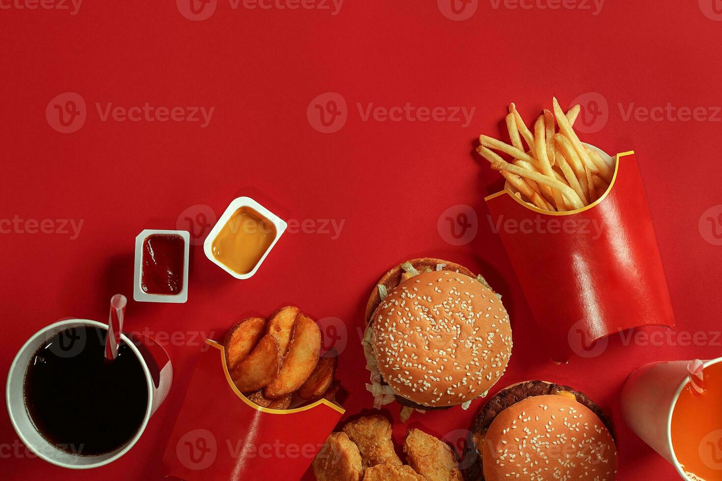 Two hamburgers and french fries, sauces and drinks on red background. Fast food. Top view, flat lay with copyspace photo