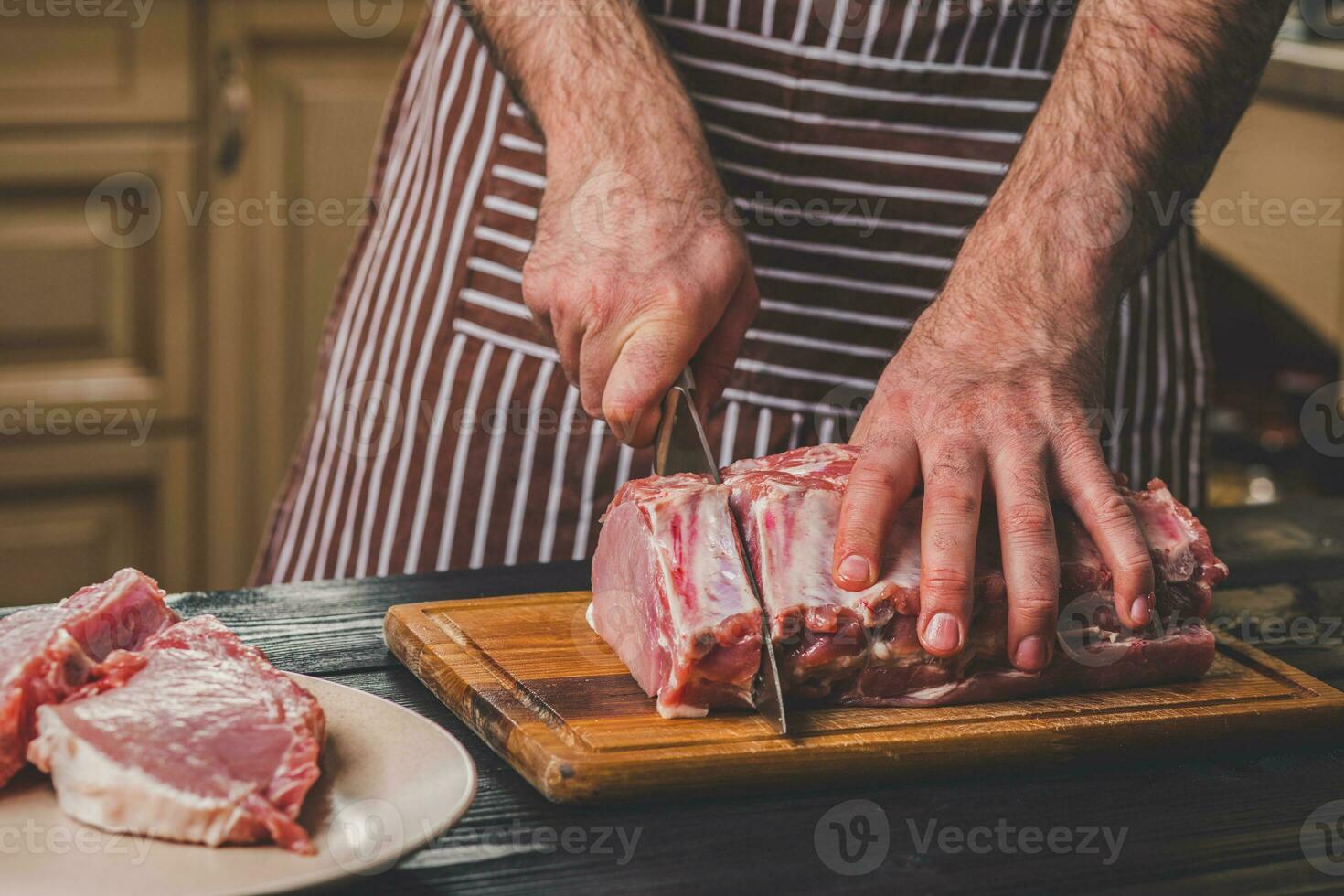 Man cuts of fresh piece of meat on a wooden cutting board in the home kitchen photo