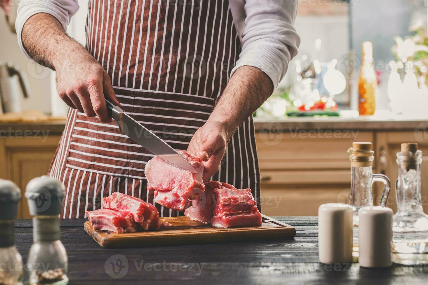 Man cuts of fresh piece of meat on a wooden cutting board in the home kitchen photo