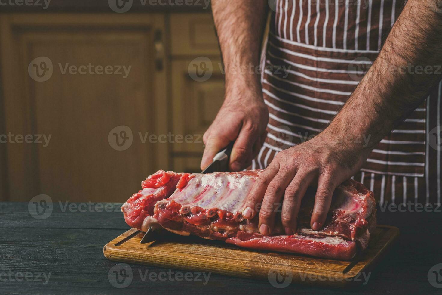 Man cuts of fresh piece of meat on a wooden cutting board in the home kitchen photo