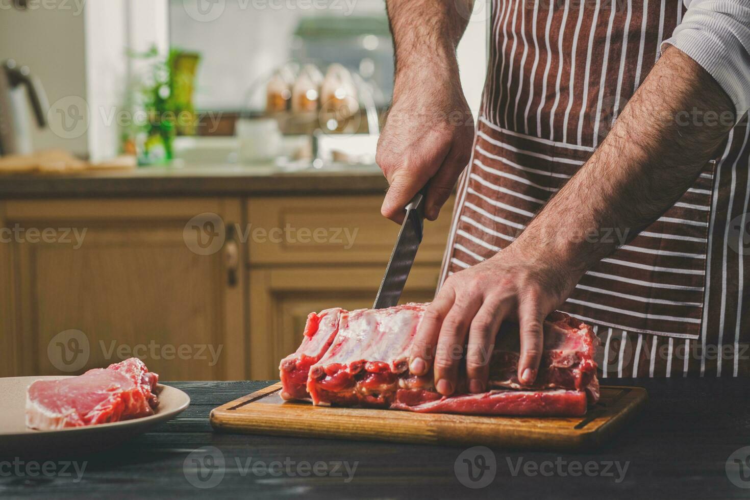 Man cuts of fresh piece of meat on a wooden cutting board in the home kitchen photo