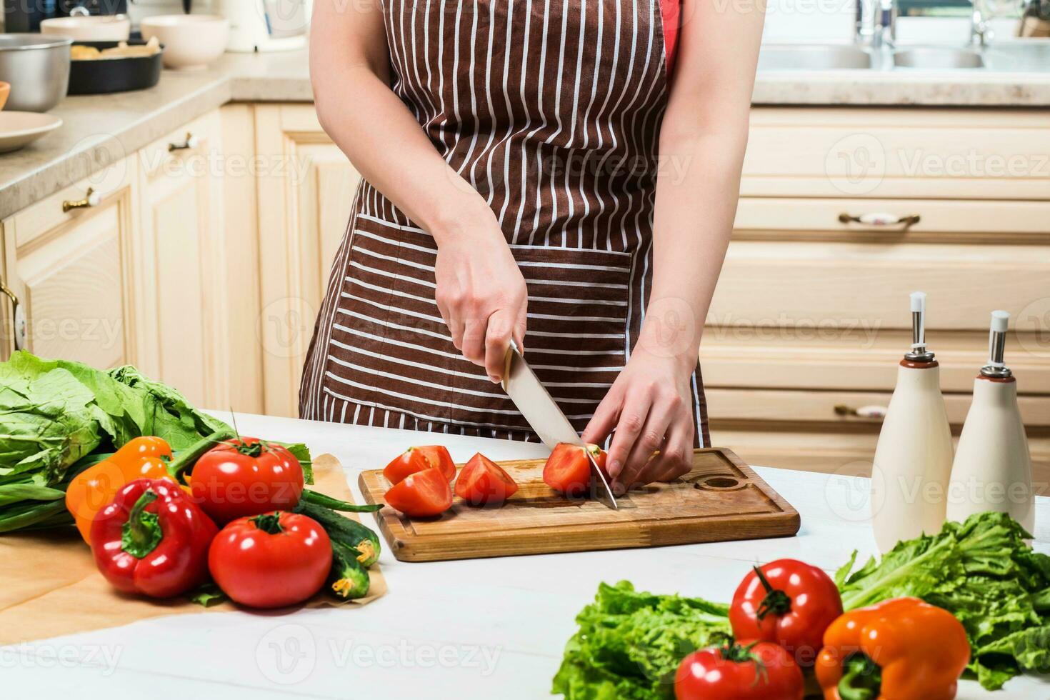 Young woman cooking in the kitchen at home. A woman cuts a tomato and vegetables with a knife. photo