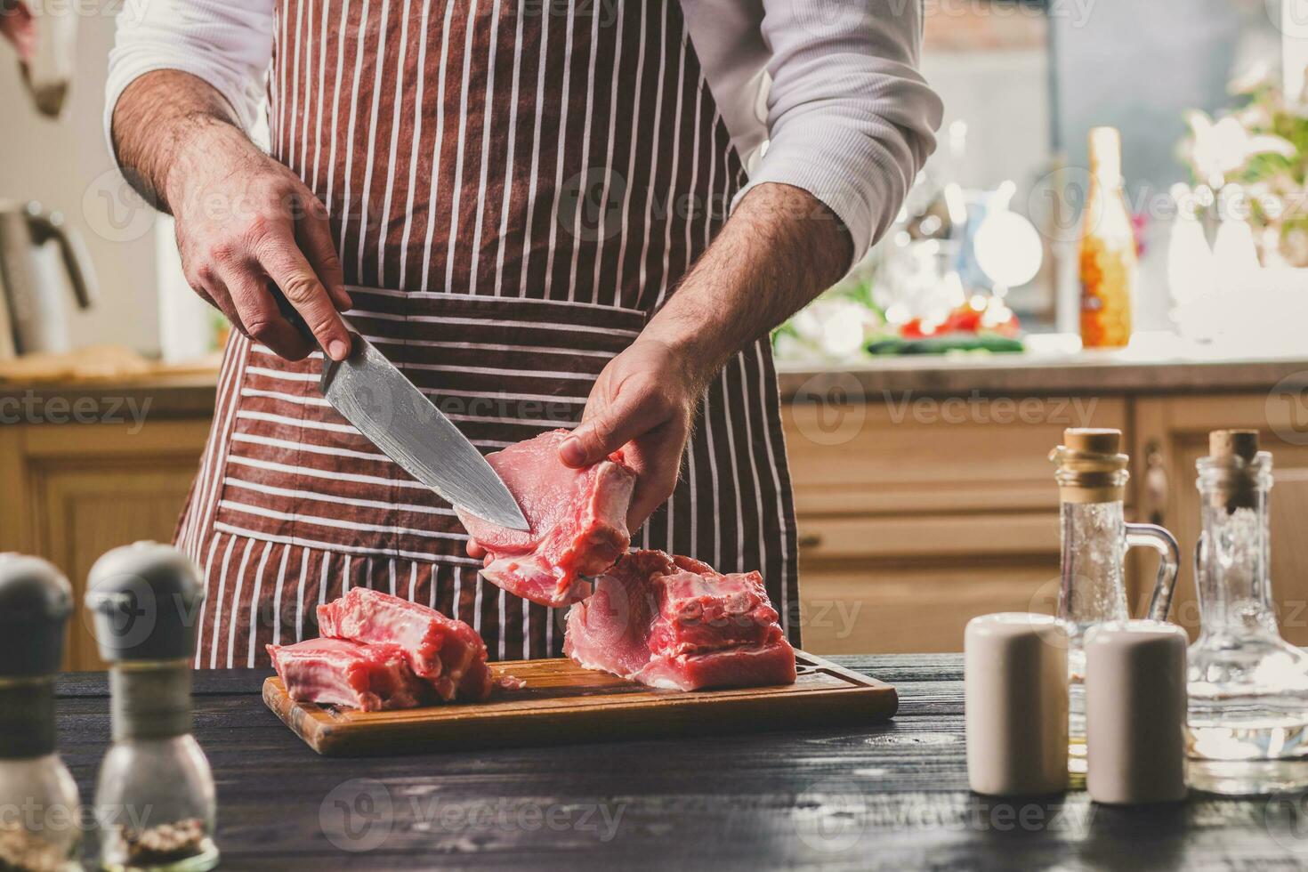 Man cuts of fresh piece of meat on a wooden cutting board in the home kitchen photo