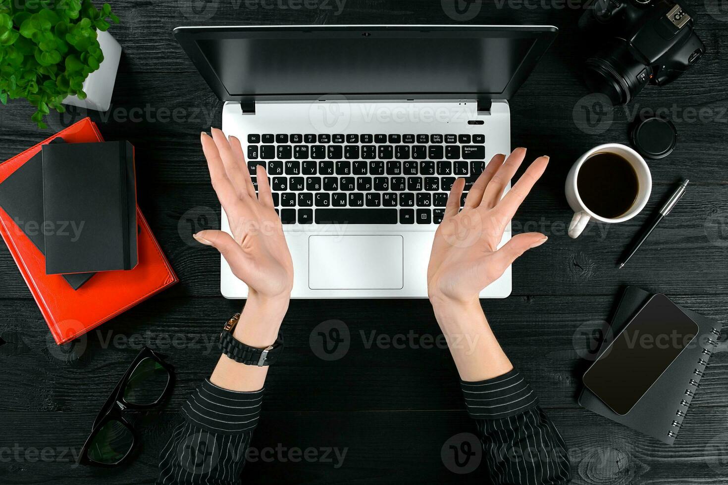 mujer trabajando a el oficina mesa. parte superior ver de humano manos, ordenador portátil teclado, un taza de café, teléfono inteligente, cuaderno y un flor en un de madera mesa antecedentes foto