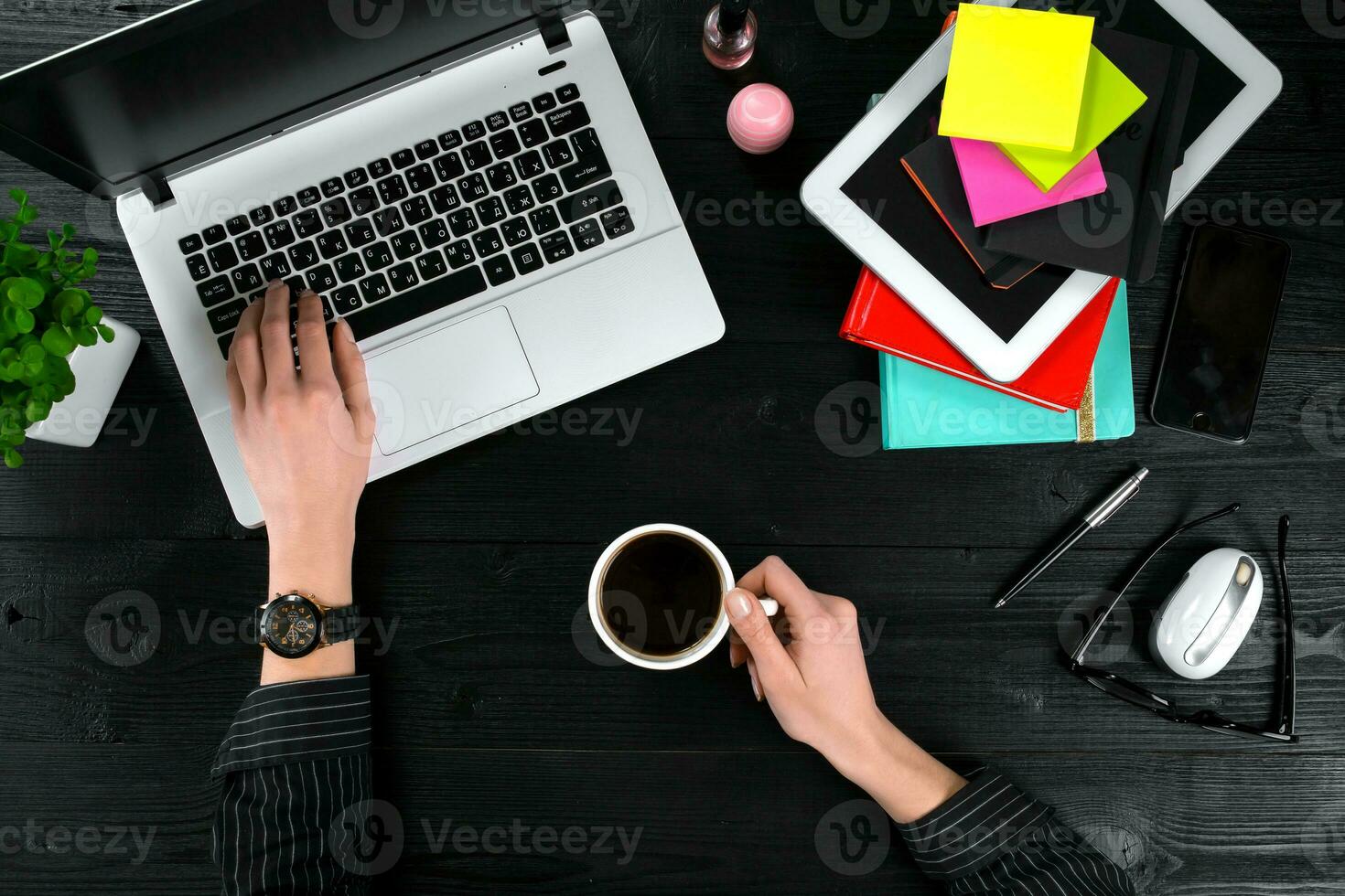 Female hands holding a cup of coffee and typing on the keyboard of a laptop on black wooden table. photo