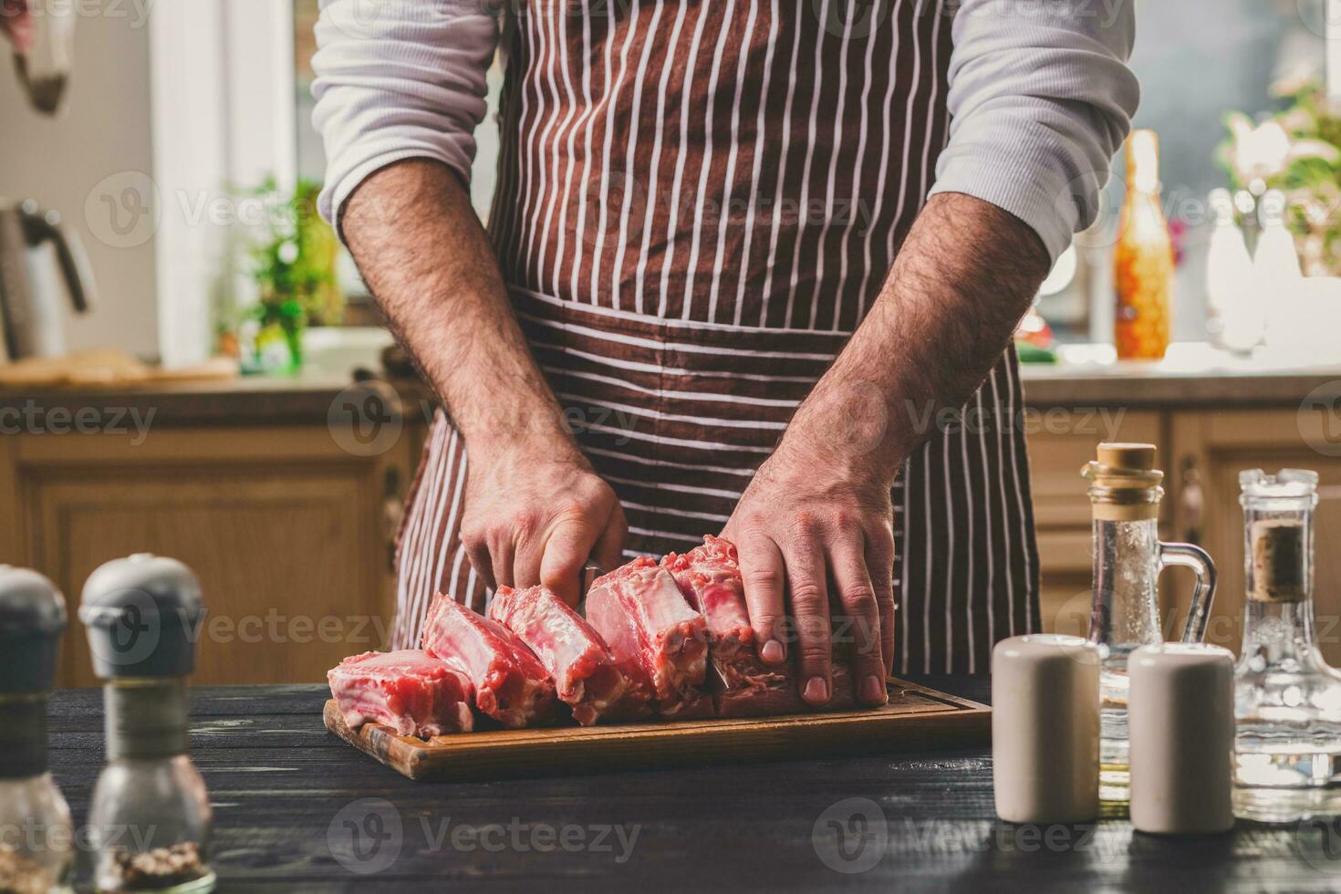 Man cuts of fresh piece of meat on a wooden cutting board in the home kitchen photo