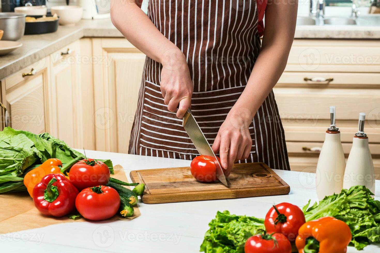 Young woman cooking in the kitchen at home. A woman cuts a tomato and vegetables with a knife. photo