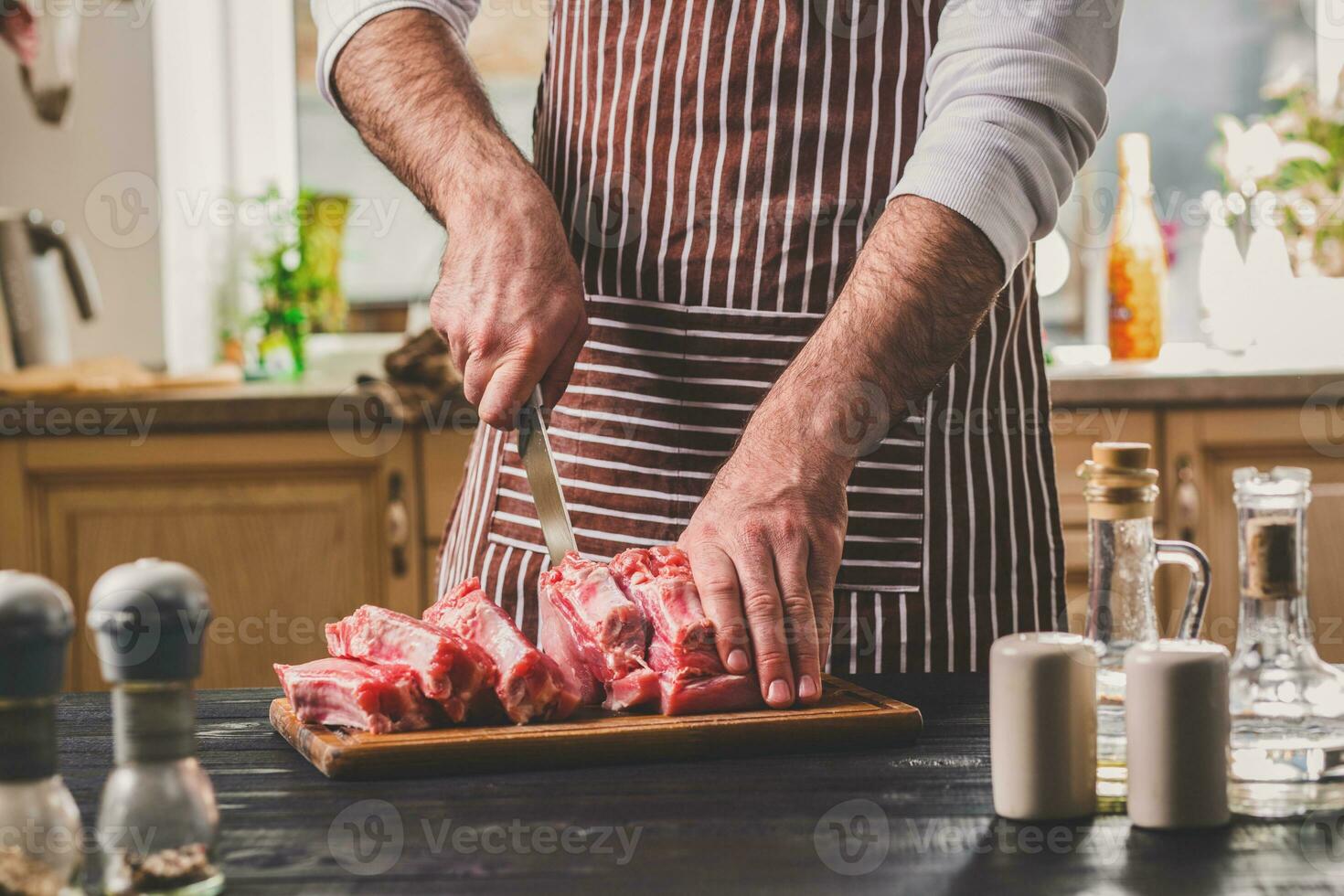 Man cuts of fresh piece of meat on a wooden cutting board in the home kitchen photo