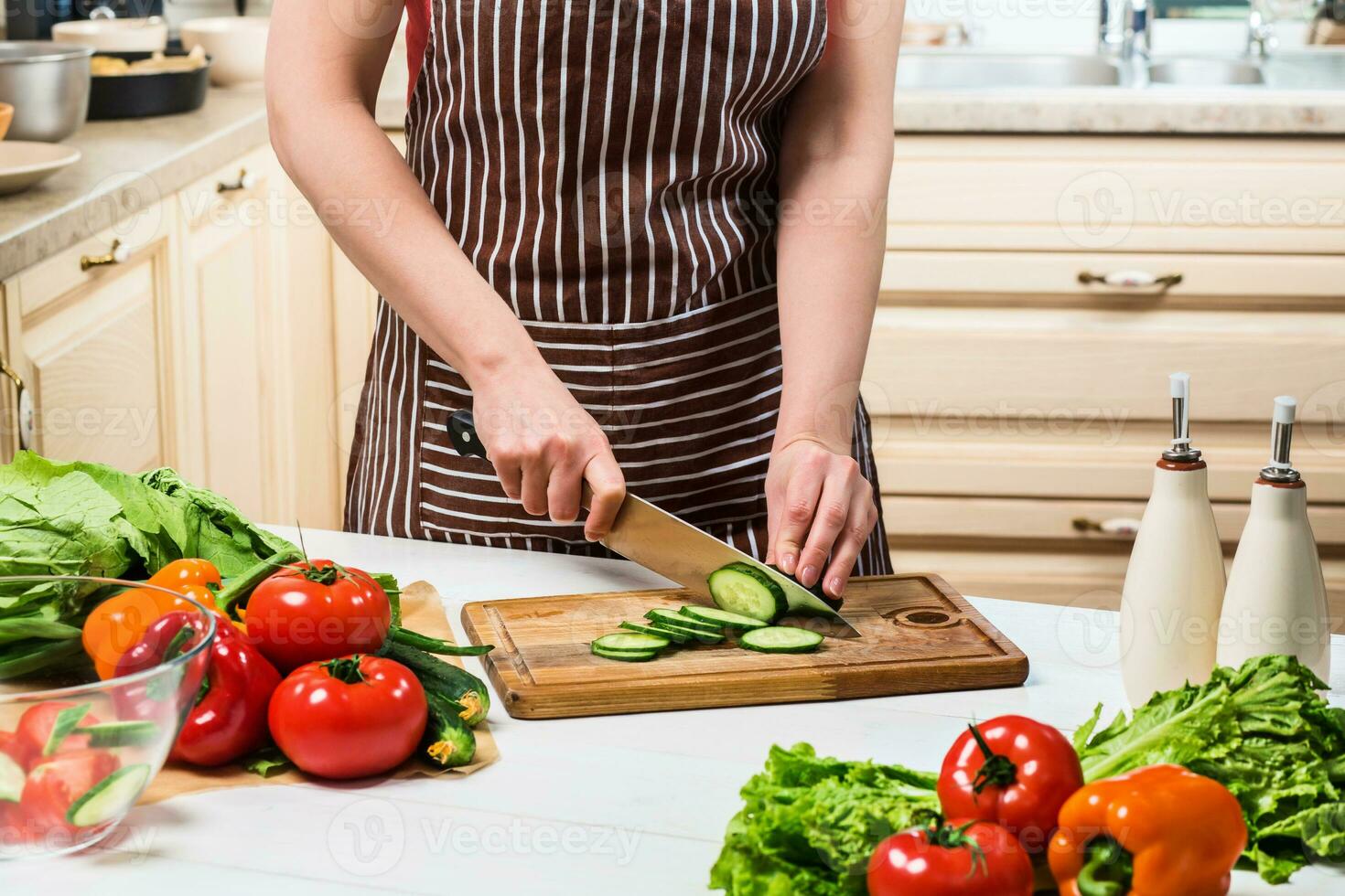 Young woman cooking in the kitchen at home. A woman cuts a cucumber and vegetables with a knife. photo