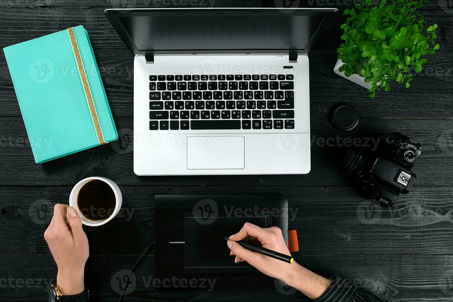Female hands holding a cup of coffee and typing on the keyboard of a laptop on black wooden table. photo