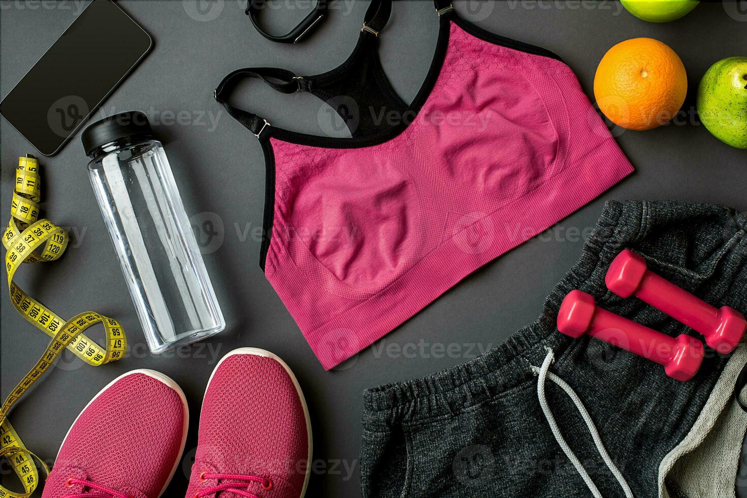 Athlete's set with female clothing, sneakers and bottle of water on gray background photo