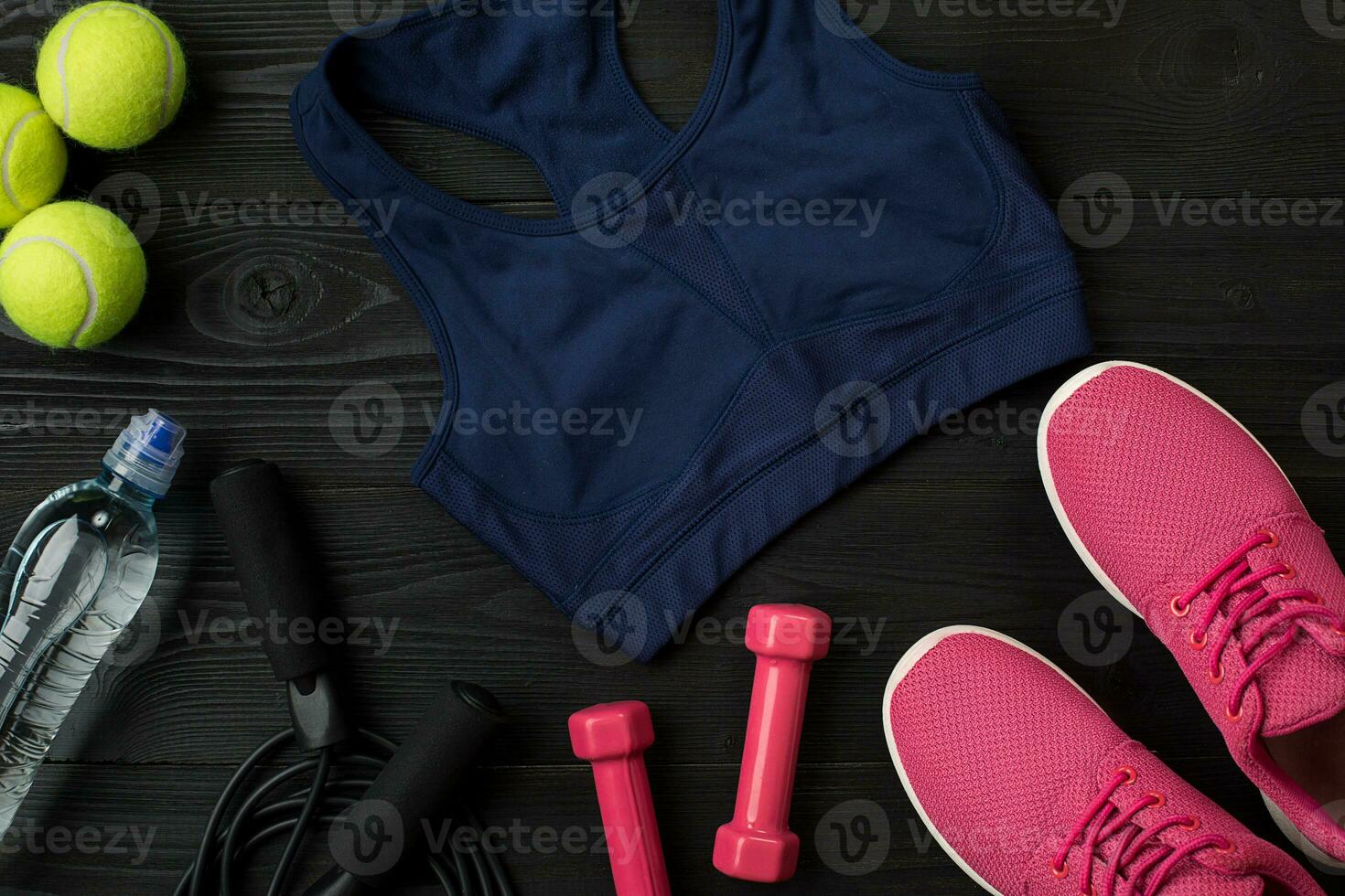 Athlete's set with female clothing, sneakers and bottle of water on dark background photo