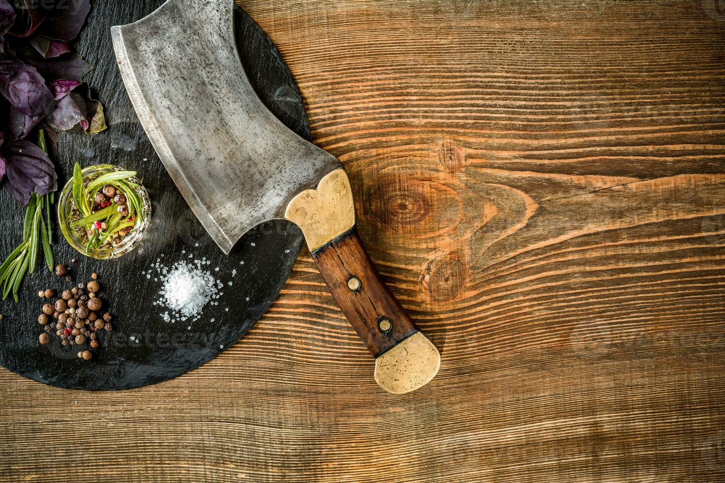 Basil and a sprig of rosemary with ax for meat on wooden background. Top view photo