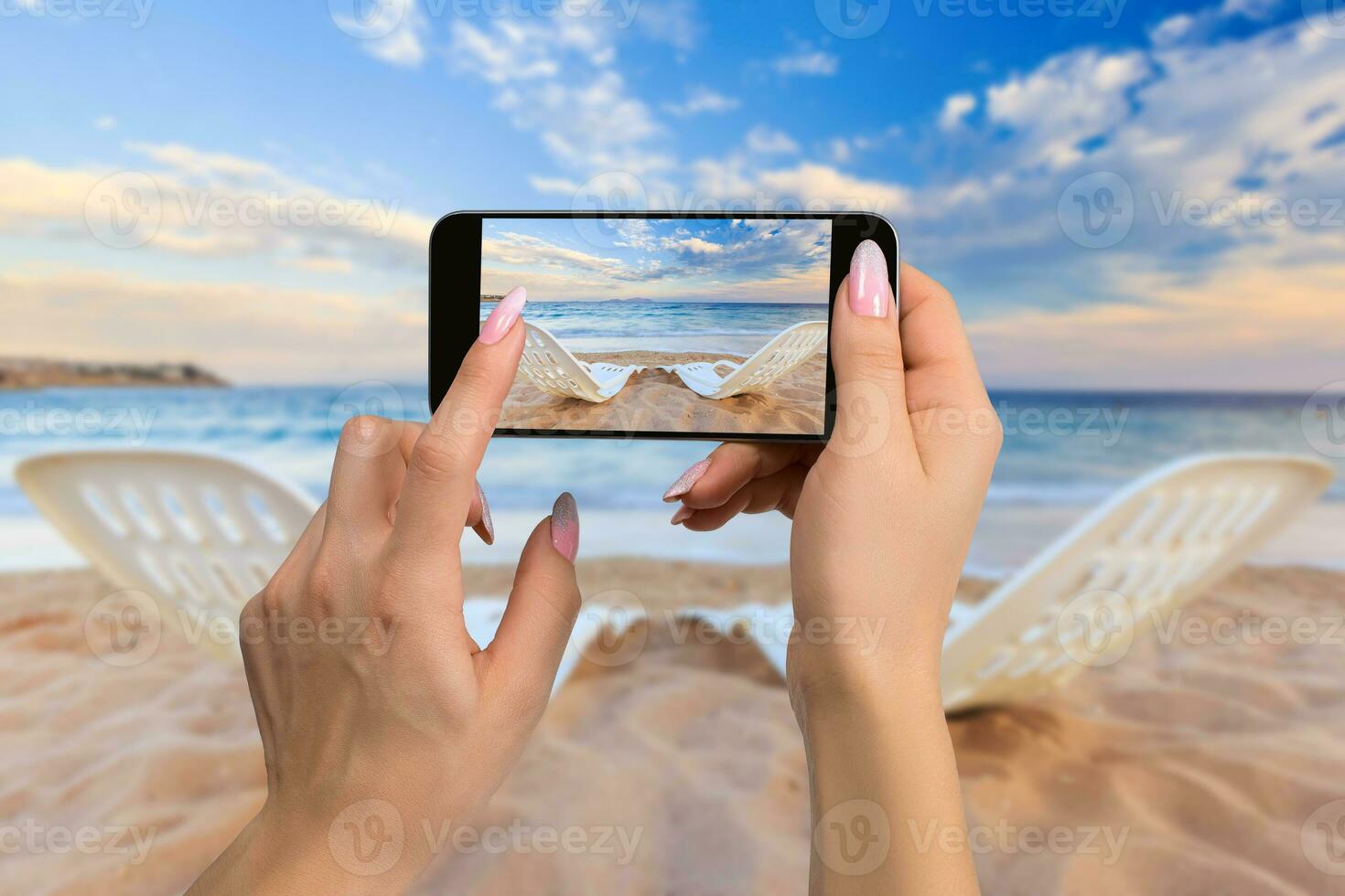 Photographing travel concept - woman takes picture of two beach chairs on the sand near sea and colorful sky photo