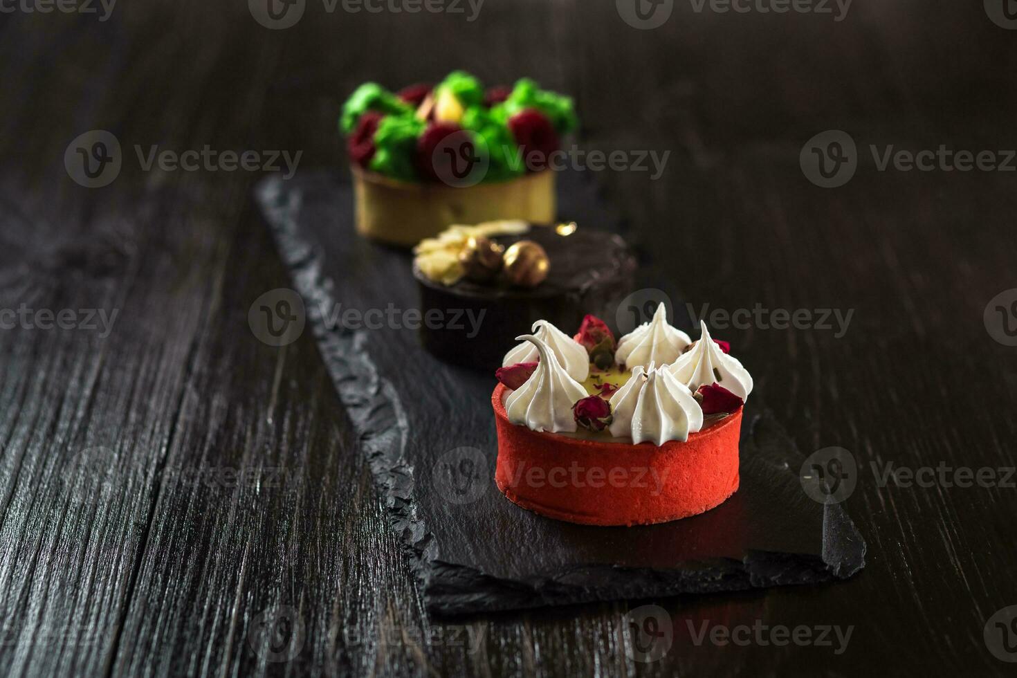 Side view on mini party tartlets with fresh fruit, chocolate, nuts and cream on black slate background photo