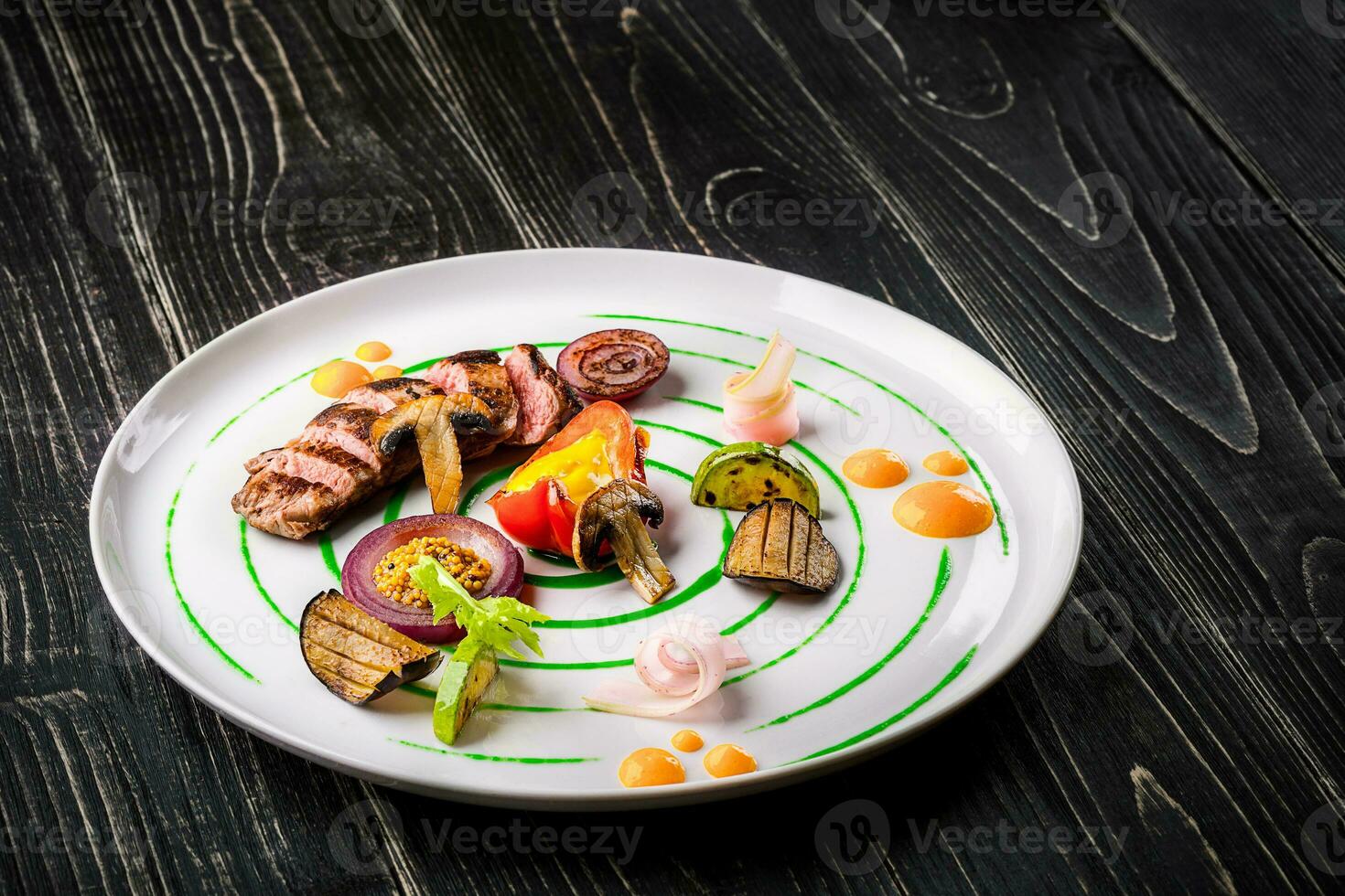 Sliced meat with fresh herbs, vegetables and spices on a white plate on a black wooden background, top view photo