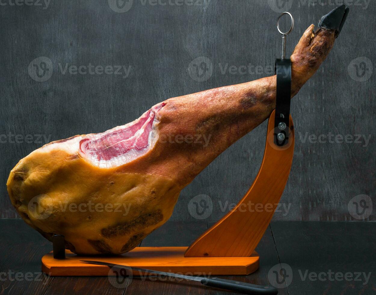 Whole mediterranean traditional jamon on a wooden stand with a knife lean on a table. Dark image photo