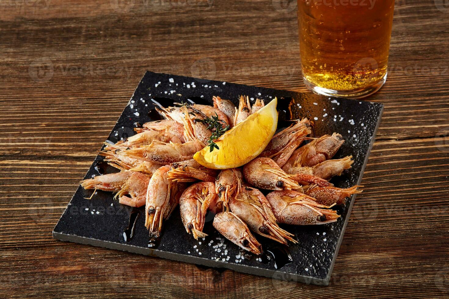 Grilled shrimps on black board pan and beer on wooden table photo