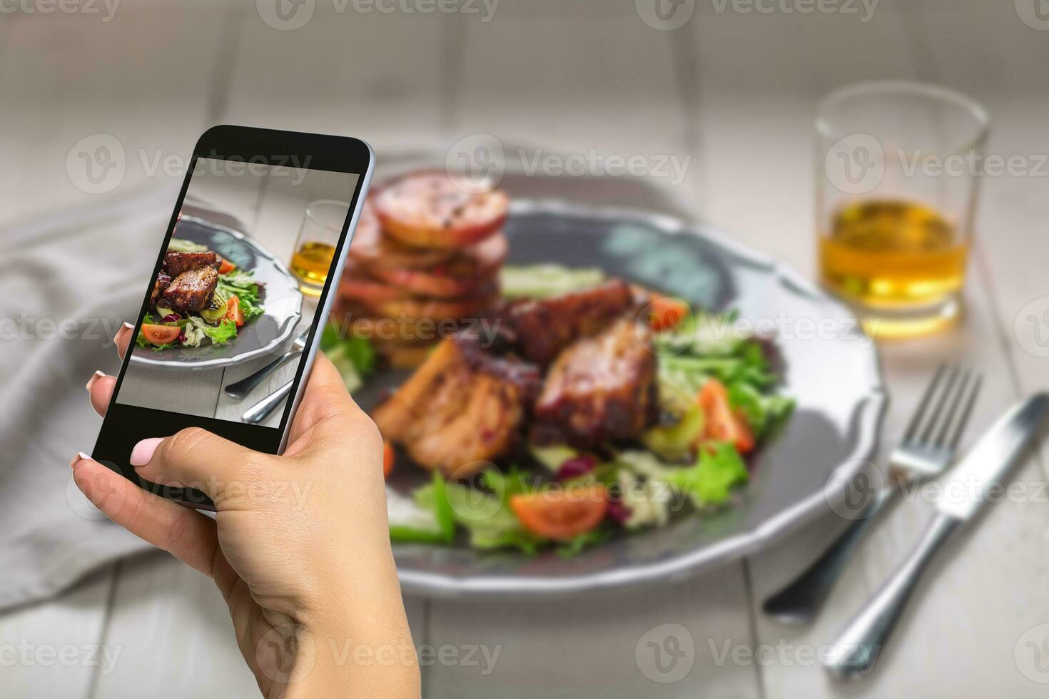 Photographing food concept - woman takes picture of hot meat dishes. Pork ribs grilled with salad and apples on a plate. photo