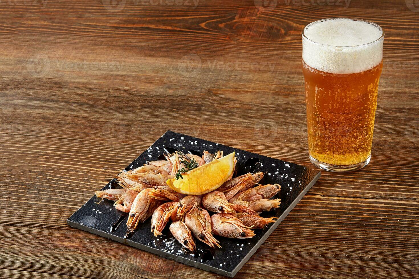 Grilled shrimps on black board pan and beer on wooden table photo