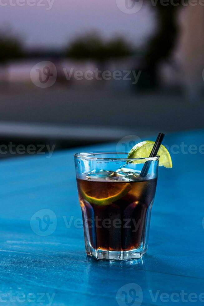 Rum cola casual cocktail with ice cubes and lime at summer bar stand background. photo