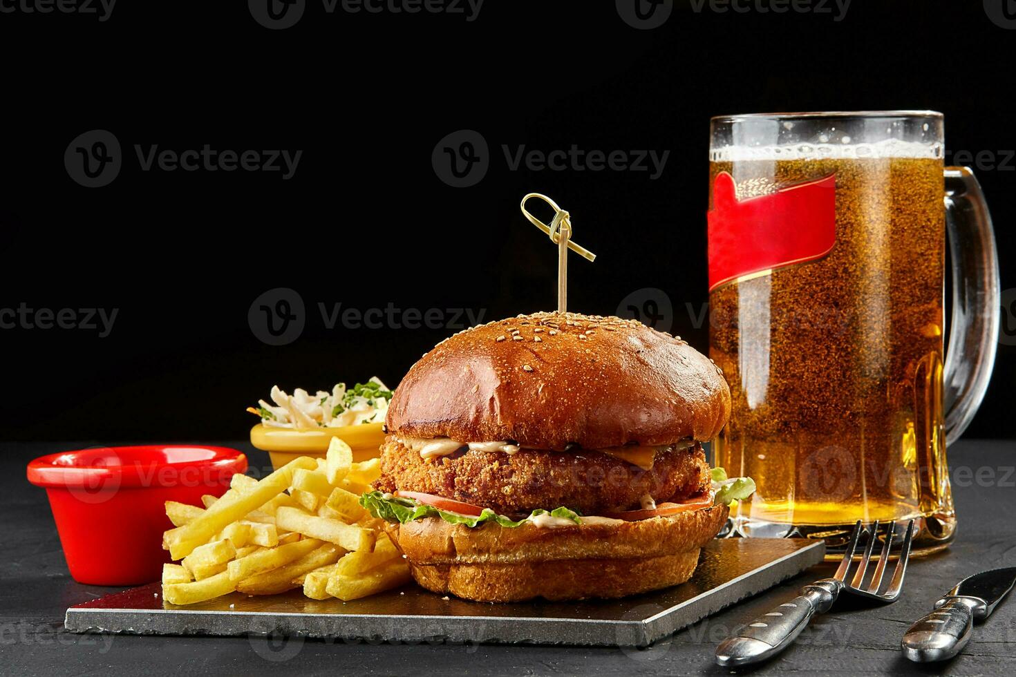 Tasty burger, french fries with sauce and glass of beer on black board photo