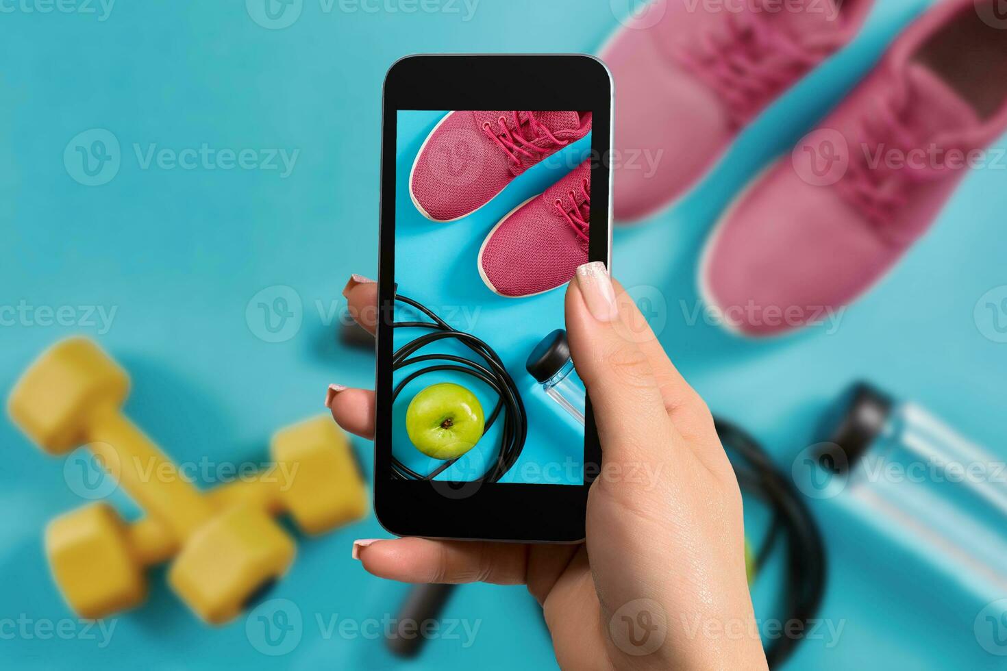 Female hand with a smartphone makes a photo fitness equipment on blue background