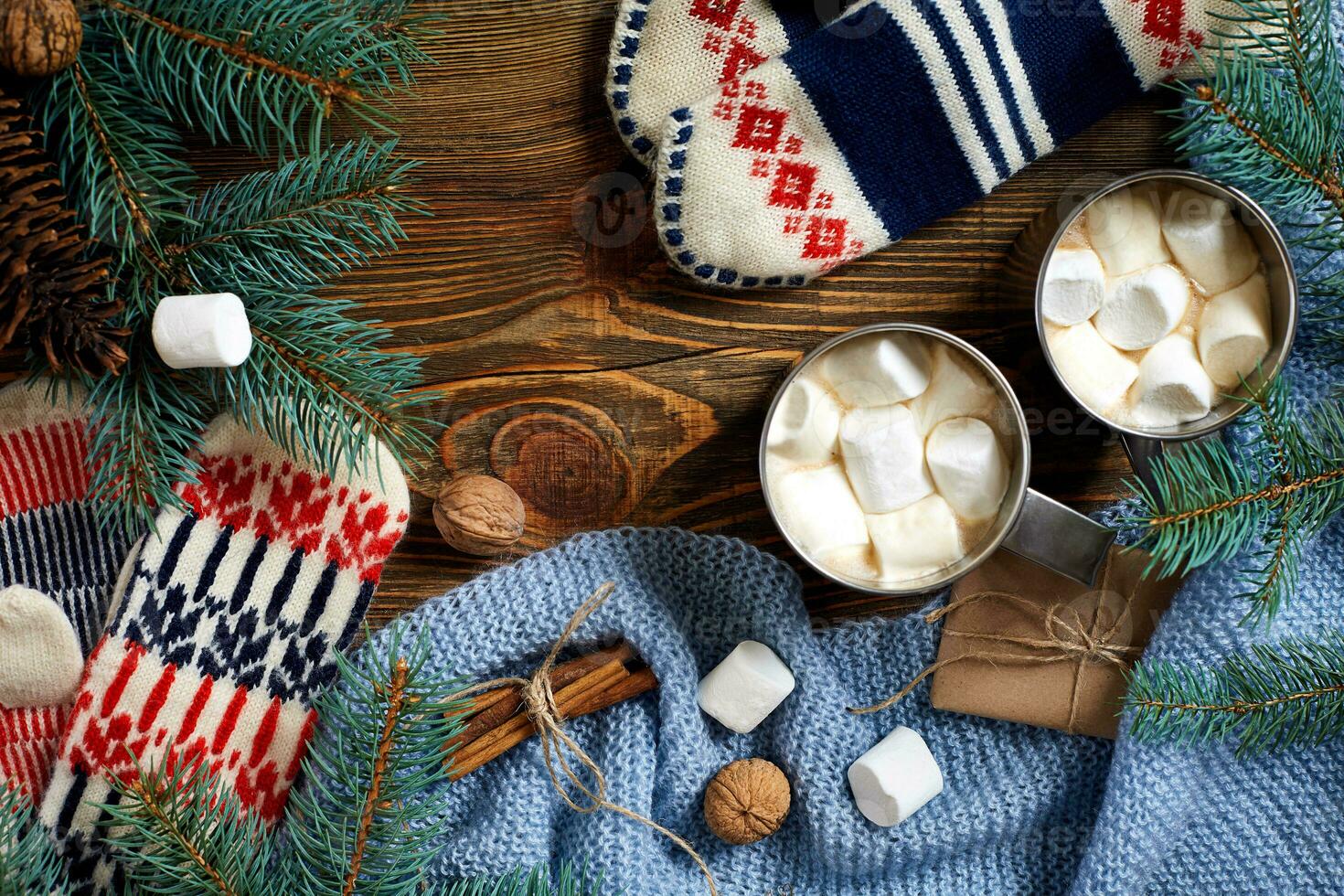 Two cups of hot cocoa or chocolate with marshmallow, mittens, christmas decor and fir tree on wooden rustic background from above. photo