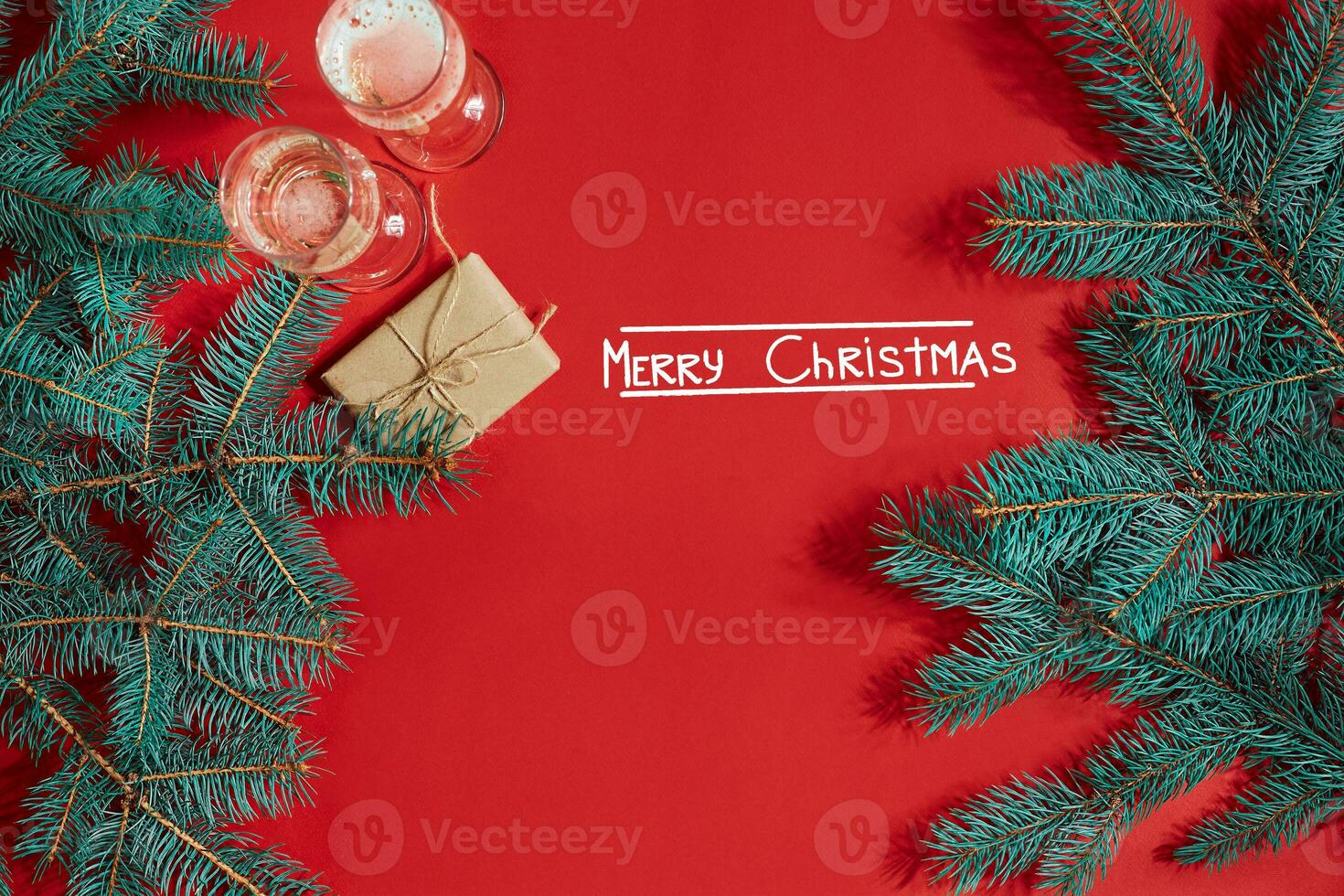 Two glasses of champagne with Christmas tree branch and small gift on a red background photo