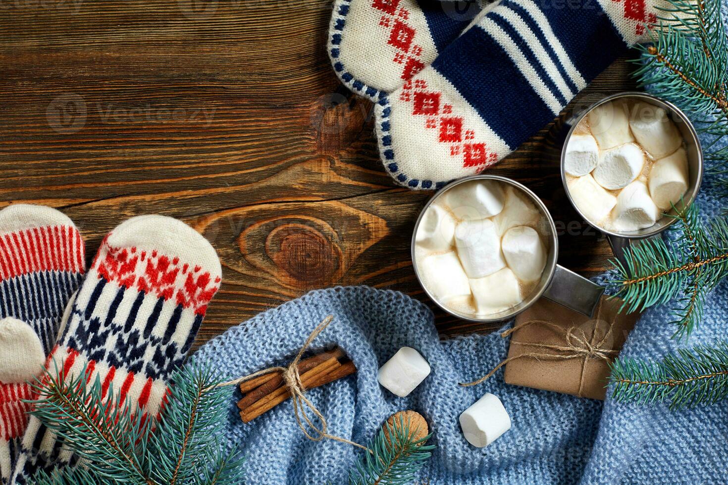 Two cups of hot cocoa or chocolate with marshmallow, mittens, christmas decor and fir tree on wooden rustic background from above. photo