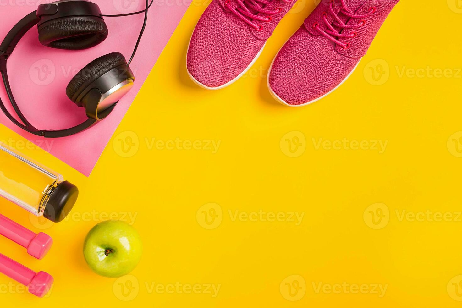 Fitness accessories on a yellow background. Sneakers, bottle of water, earphones and dumbbells. photo